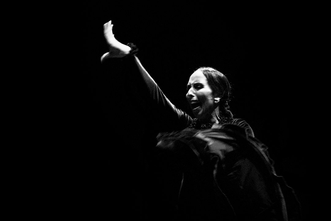 Una bailarina alza un brazo sobre un fondo oscuro.